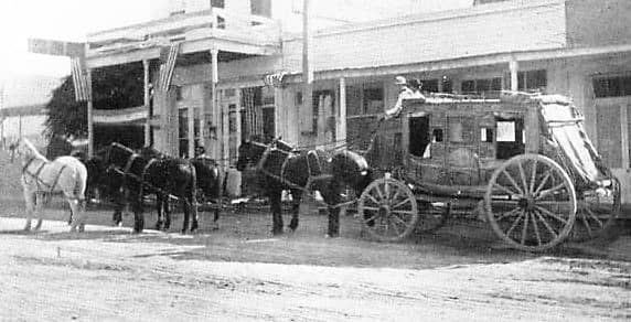 A 6-team horse stagecoach pulling up to a historic stagecoach inn.